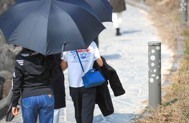  추위가 풀려 포근한 날씨를 보이는 5일 오후 제주시 애월읍 한담해안산책로에서 우산을 쓴 관광객들이 가벼운 옷차림으로 걸어가고 있다. (사진=뉴시스 제공)