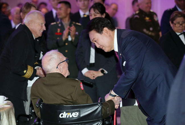 윤석열 대통령이 25일(현지시간) 워싱턴DC 한 호텔에서 열린 한미동맹 70주년 기념 오찬에 입장하며 참전용사인 랄프 퍼켓 예비역 육군 대령의 손을 잡고 대화하고 있다.(사진=뉴시스 제공)