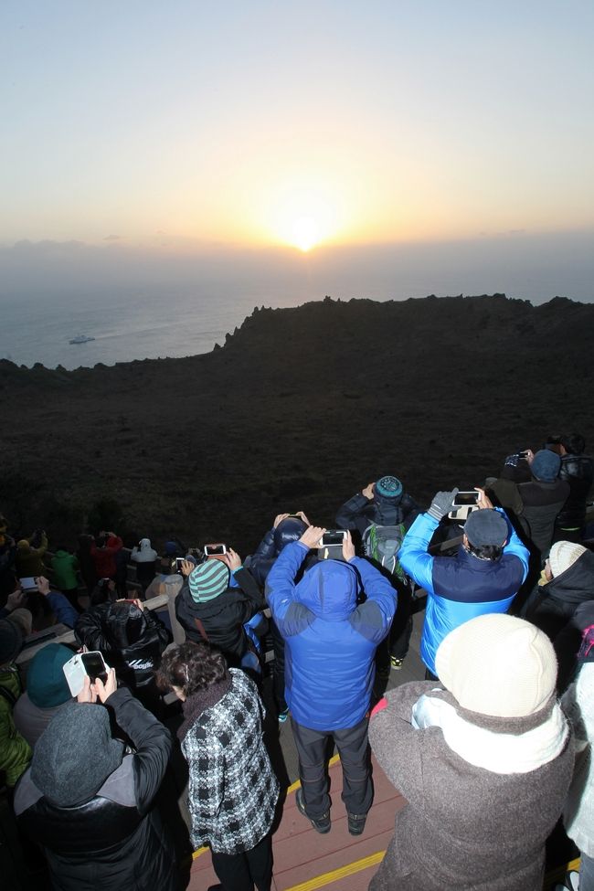 성산일출봉을 찾은 관광객들이 구름 위로 떠오르는 해를 핸드폰에 담고 있다.