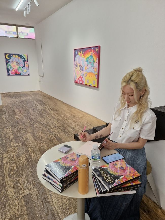 이사라 작가가 전시 오프닝에 출간된 판타지 아트 소설 'What Happened in the Wonderland’에 사인하고 있다. <사진=이화순>